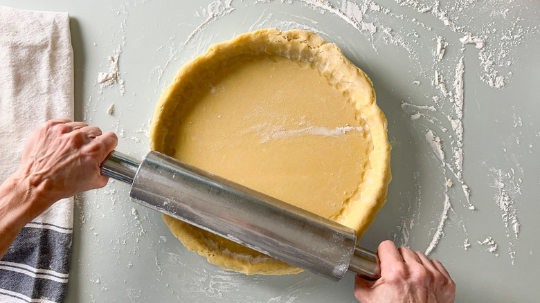 Trimming quiche dough on tart pan with rolling pin