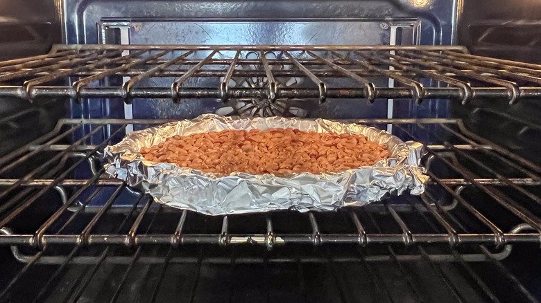 Dried beans on foil wrapped quiche shell baking in tart pan in oven