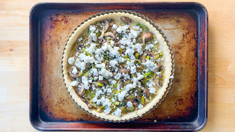 Leeks, mushrooms, and goat cheese in baked quiche shell on baking sheet