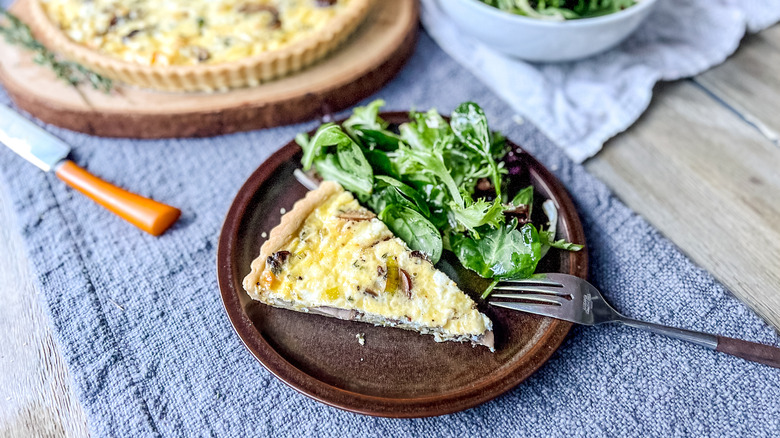 Mushroom and leek quiche slice on plate with greens