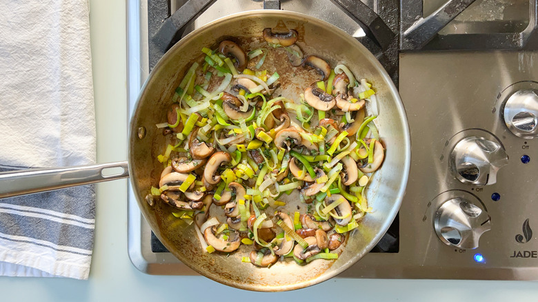Sliced mushrooms, leeks, and thyme in saute pan on stove