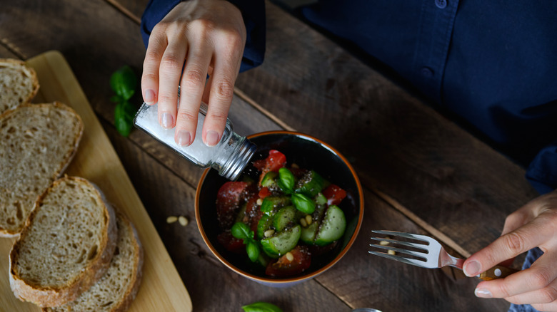 Person sprinkling salt on salad