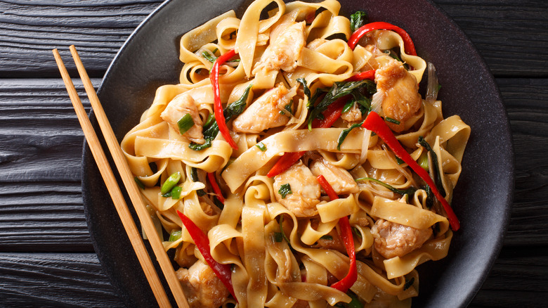 A plate of drunken noodles on a wooden table