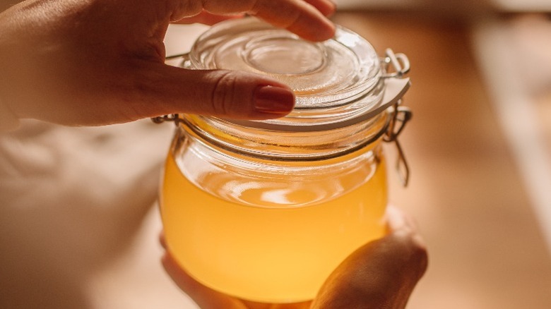 Hands holding a wire-clip-lid jar filled with clarified butter