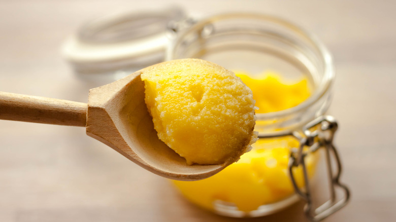 Ghee scooped in a wooden spoon with a jarful in the background