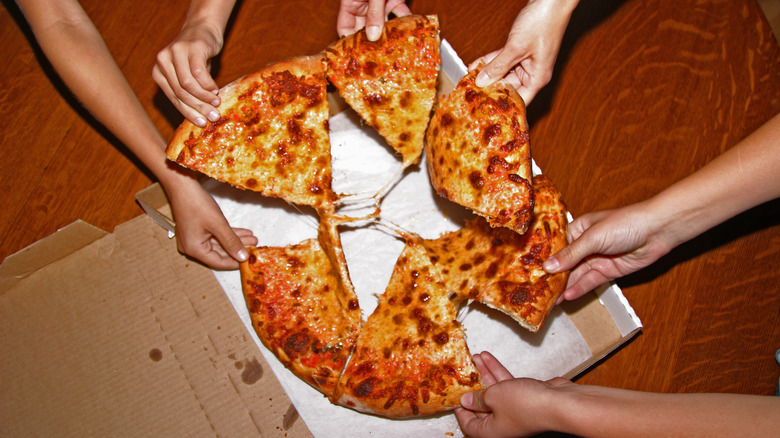 People grabbing pizza from a pizza box