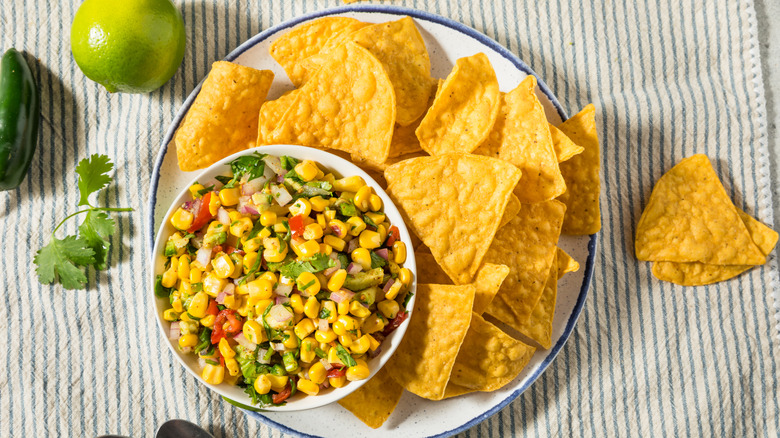 Corn Salsa in a white bowl with Tortilla Chips, lime and cilantro scattered around