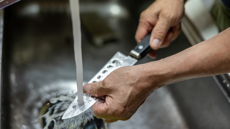 Hand washing chef knife in a metal sink