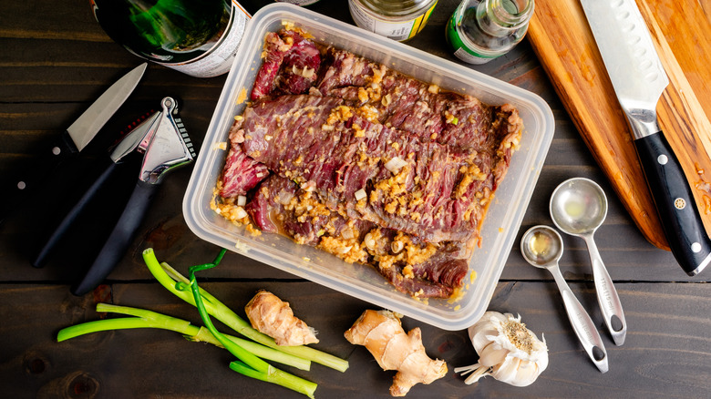 Marinating steak in a plastic container surrounded by ingredients and kitchen tools