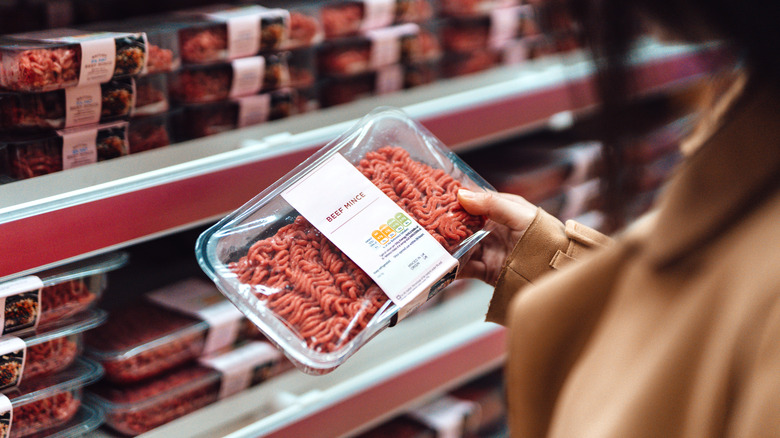 A woman holding a package of ground beef at the store