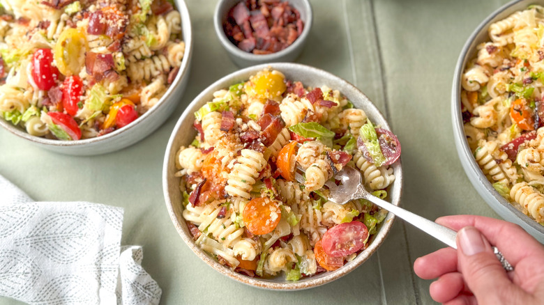 Bowls of over-the-top BLT pasta salad on table with chopped bacon garnish