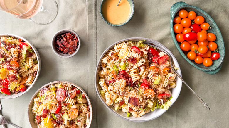 Over-the-top BLT pasta salad in bowls on table with garnishes