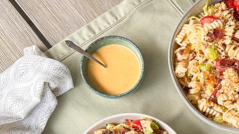 Bacon mayo dressing in serving bowl on table with over-the-top BLT pasta salad