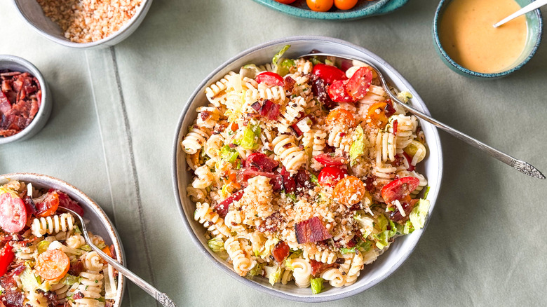 Over-the-top BLT pasta salad in serving bowls on table with bacon mayo dressing