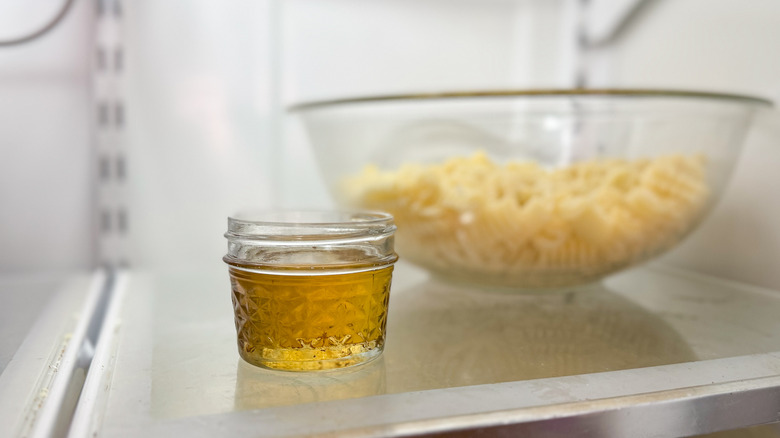 Small jar of rendered bacon fat in refrigerator with pasta in bowl