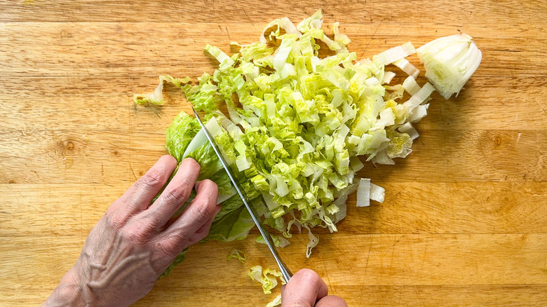 Chopping romaine lettuce on cutting board with chef's knife