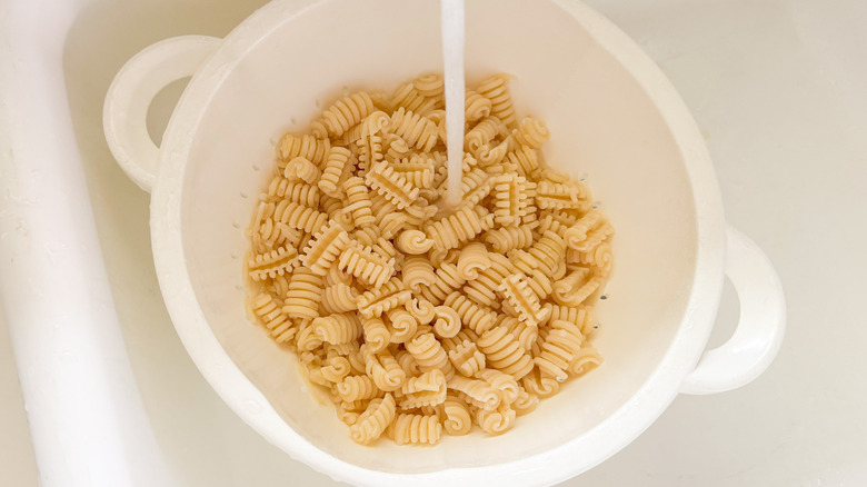 Radiatore pasta being rinsed with water in colander in sink