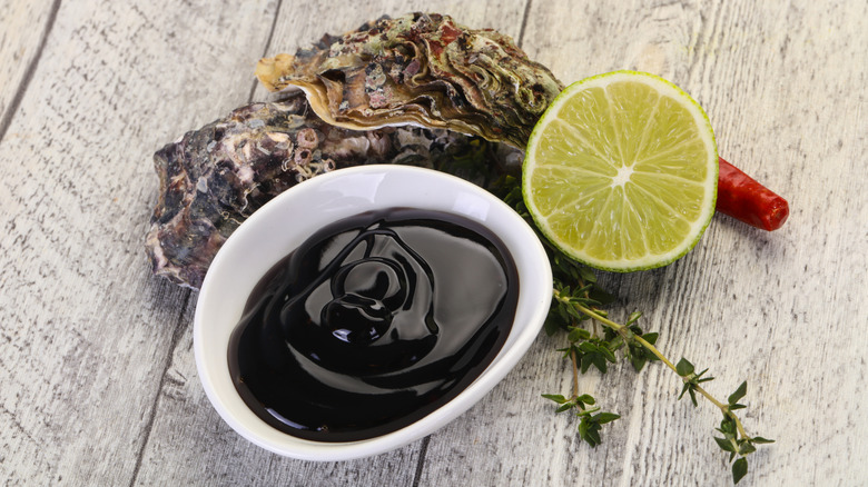 A bowl of oyster sauce with an oyster and a lime.