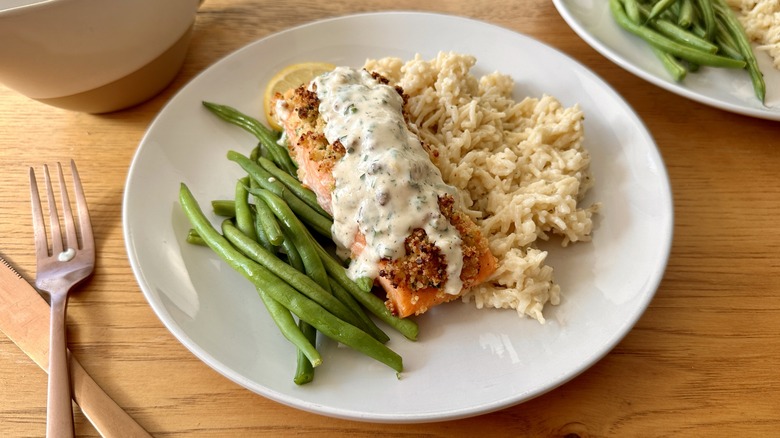 salmon with white sauce, rice, and green beans on a white plate