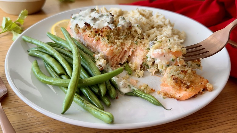 salmon with white sauce, rice, and green beans on a white plate