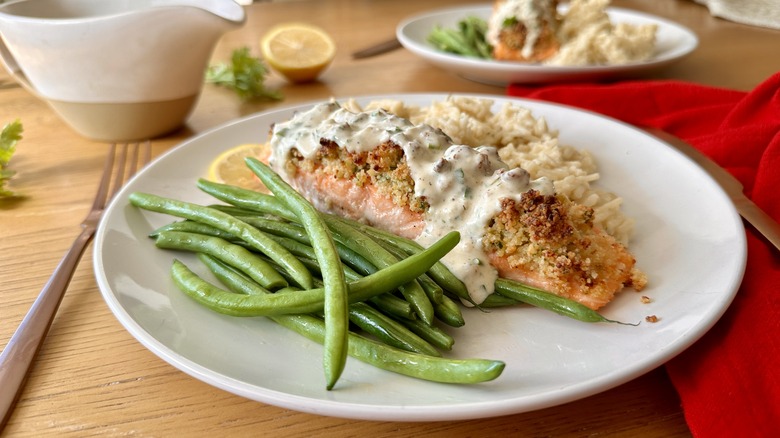 salmon with white sauce, rice, and green beans on a white plate