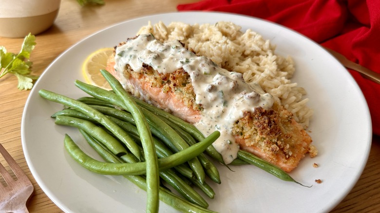 salmon with white sauce, rice, and green beans on a white plate