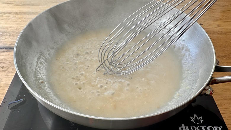 beige liquid in a metal frying pan with a whisk