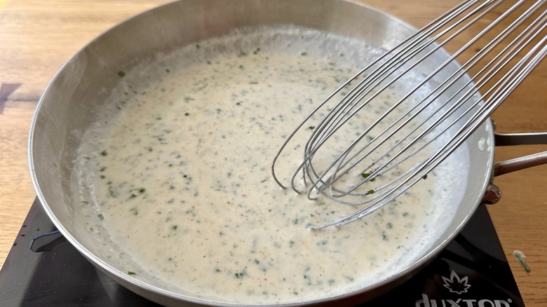 white sauce with herbs in a metal frying pan with a whisk