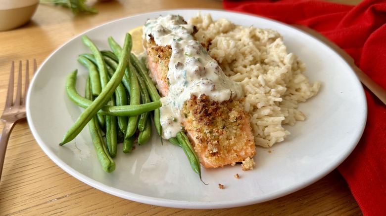 salmon with white sauce, rice, and green beans on a white plate