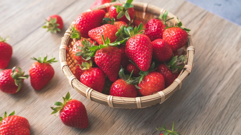 A woven basket filled with strawberries on wooden table