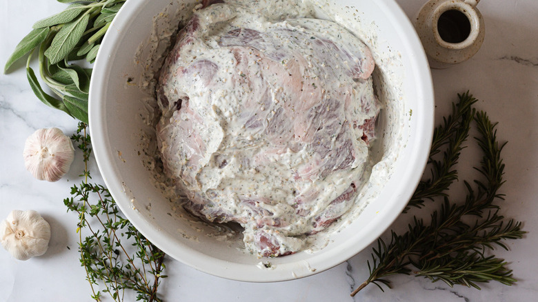 marinated lamb in white bowl with herbs around