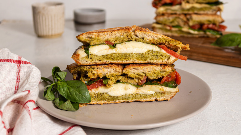 Two halves pesto caprese panini stacked on top of one another served on a plate