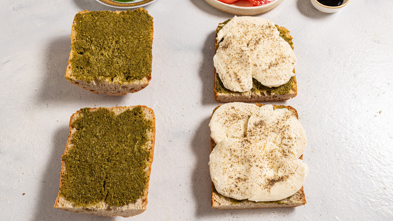 Four slices of bread, two with pesto and two with mozzarella on top