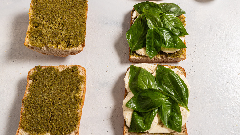 Four slices of bread, two with pesto and two with mozzarella and fresh basil on top