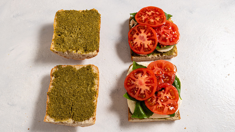 Four slices of bread, two with pesto and two with mozzarella, fresh basil, and tomato slices on top