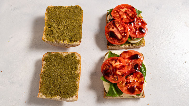Four slices of bread, two with pesto and two with mozzarella, fresh basil, tomato slices, and balsamic on top