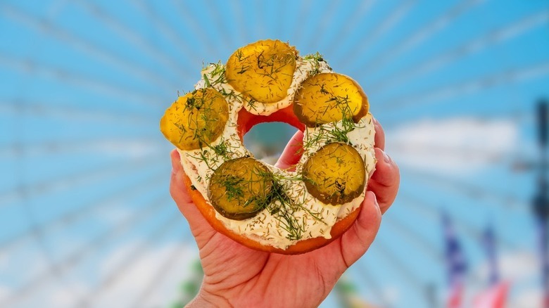 Hand holding a pickle donut in front of a ferris wheel