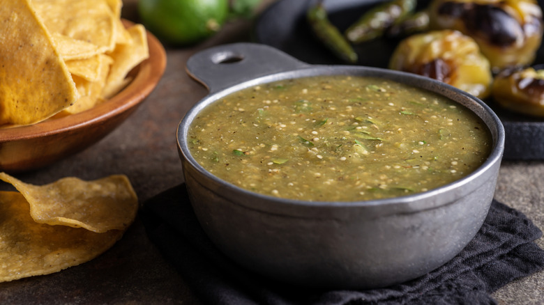 A bowl of salsa verde with chips on stone background