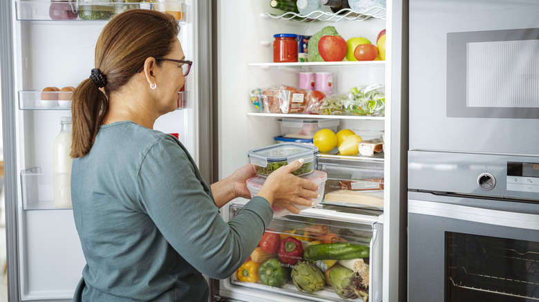 A person putting containers of food in the fridge