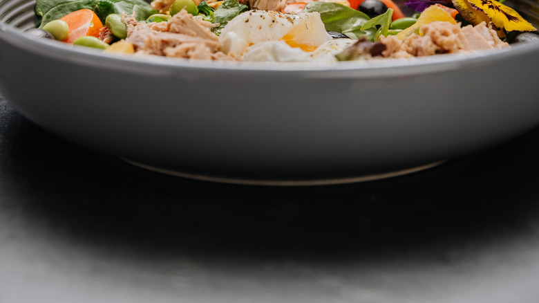 A person squeezing lemon into a bowl of tuna salad