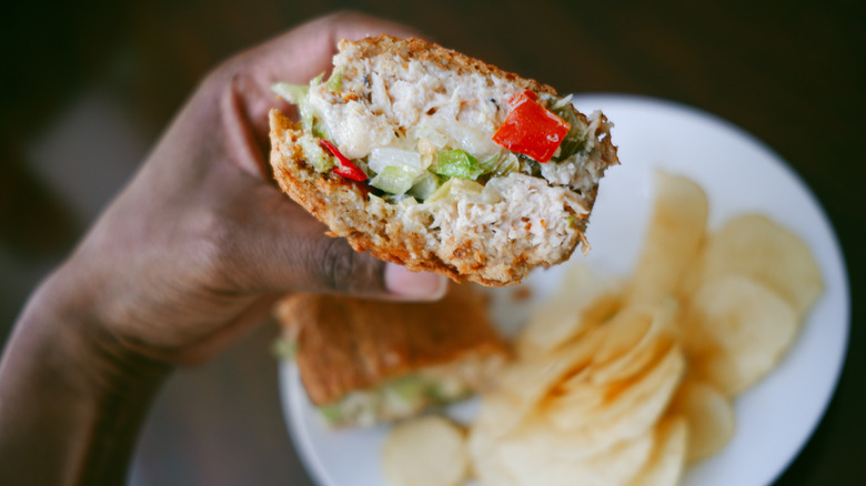 A person holding a tuna salad sandwich with diced fresh vegetables