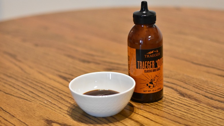 A bottle of Traeger classic barbecue sauce next to a white bowl with sample on a wooden table