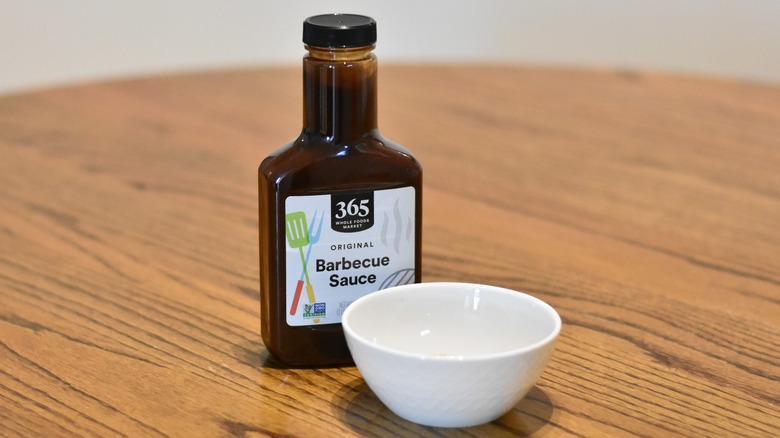 A bottle of 365 Whole Foods original barbecue sauce with a white bowl on a wooden table