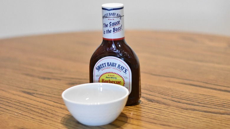 A bottle of Sweet Baby Ray's barbecue sauce next to a white bowl on a wooden table