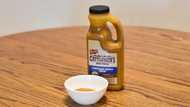 A botte of French's Cattlemen's Carolina tangy gold barbecue sauce next to a white bowl with a sample on a wooden table