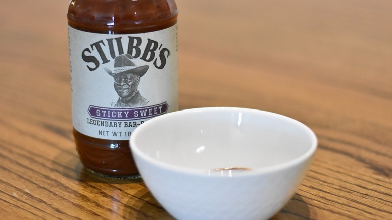 A bottle of Stubb's sticky sweet barbecue sauce behind a white bowl with sample on a wooden table