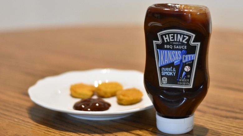 A bottle of Heinz Kansas City sweet and smoky barbecue sauce in front of a white plate with a sample and three chicken nuggets on a wooden table