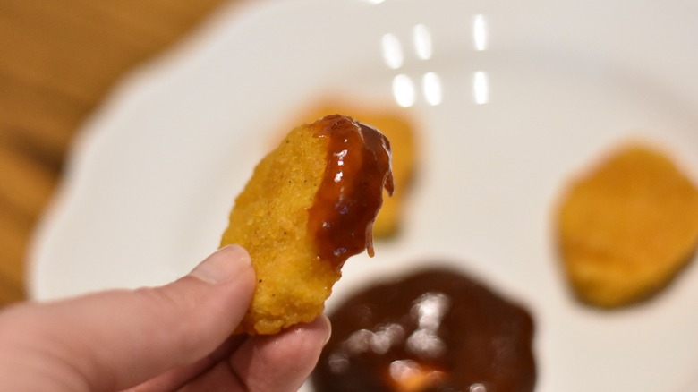 A woman dipping a chicken nugget into barbecue sauce close up