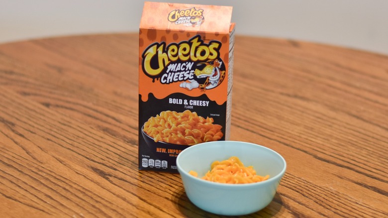 Cheetos mac and cheese box next to a blue bowl of prepared pasta spirals with cheese