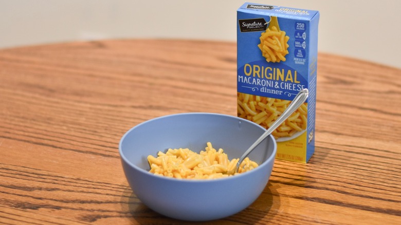 A box of Signature Select macaroni and cheese next to a blue bowl of macaroni